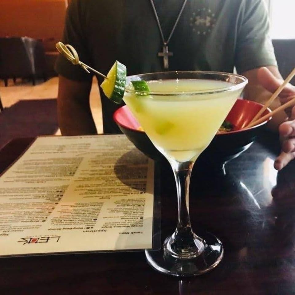 A cucumber martini with a menu and a person holding chopsticks at Leo's Asian Bistro.