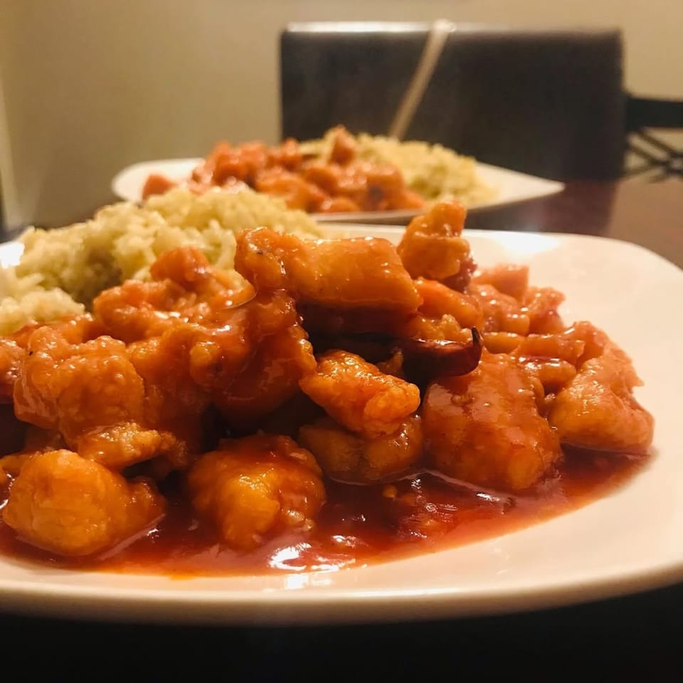 Sweet and sour chicken with rice on a white plate, with another plate in the background.